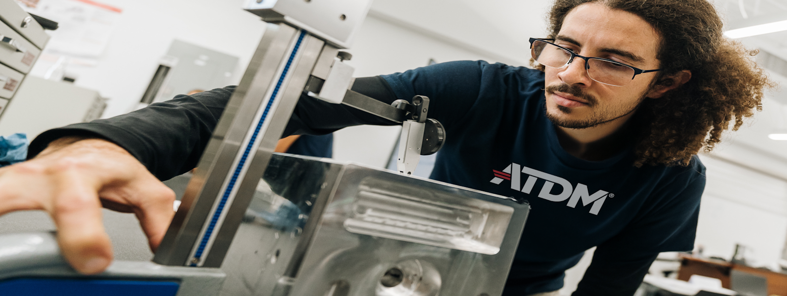A person wearing safety glasses and leaning over a machine.