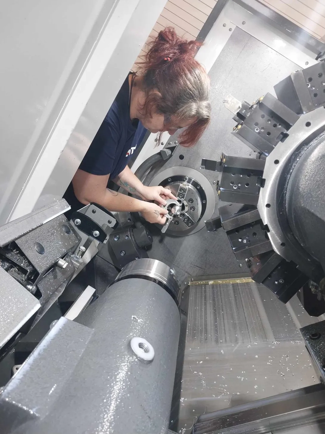 Woman leaning inside CNC lathe machine to mount item. 