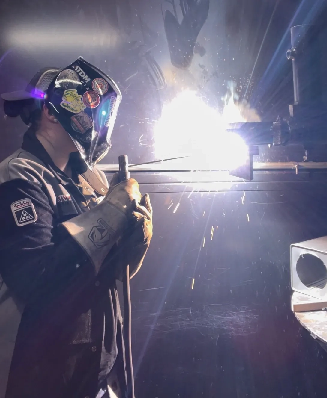 Woman standing on left welding a piece of metal on right. 