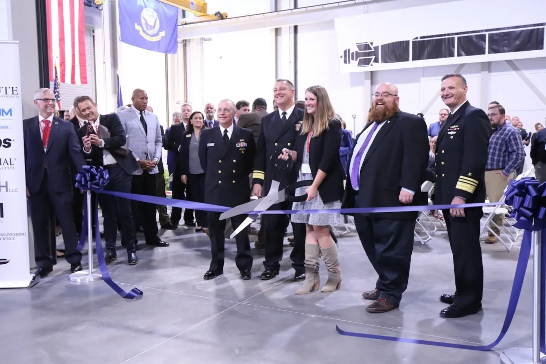 Officials holding a large pair of scissors at a ribbon cutting event
