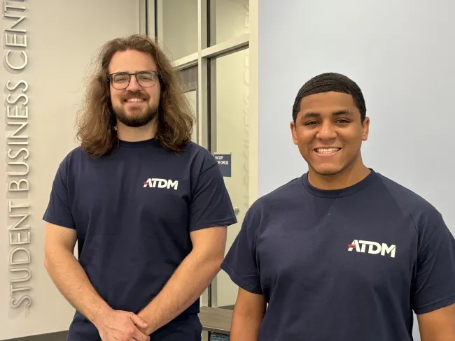 Two men stand beside each other wearing ATDM tshirts.